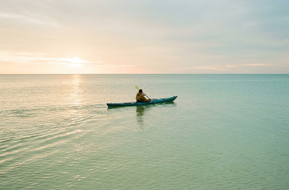 Lone kayaker paddling in turquoise waters at sunrise on Anna Maria Island winter rental destination
