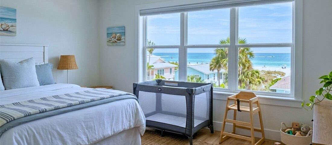 A bedroom with a large ocean-view window, furnished with a bed, a portable travel crib, and a wooden highchair.
